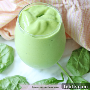 Mango Avocado Smoothie Without Banana — Creamy Tropical Drink 13 Featured image with text: mango green smoothie in a tumbler glass with spinach leaves around it and an orange linen behind it