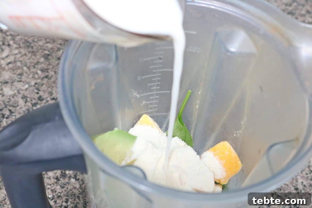 Mango Avocado Smoothie Without Banana — Creamy Tropical Drink 6 Almond milk being poured into a blender with avocados, ice, and mango
