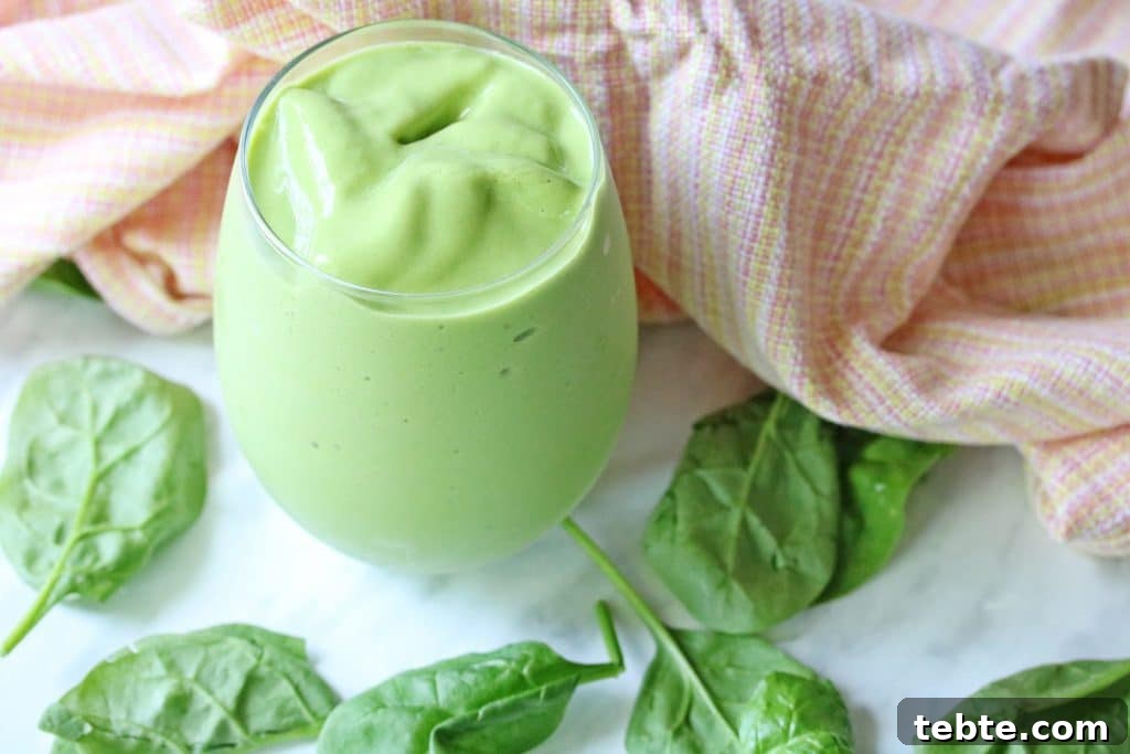Mango Avocado Smoothie Without Banana — Creamy Tropical Drink 7 A green smoothie in a glass with fresh spinach leaves and an orange linen around it