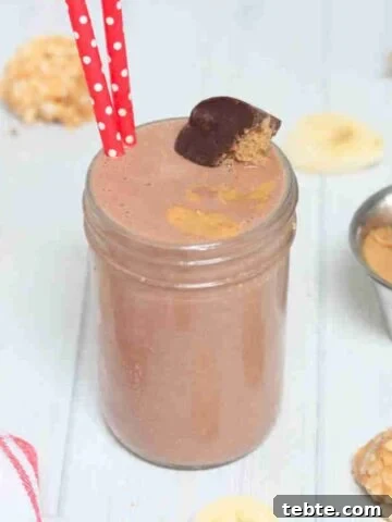 Chocolate peanut butter cup smoothie in mason jar topped with peanut butter cup and red straws in it.