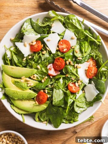A serving bowl of spinach and arugula salad with a lemon thyme vinaigrette on a butcherblock countertop.
