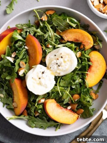 Close up of a serving of arugula burrata salad with peaches and almonds.