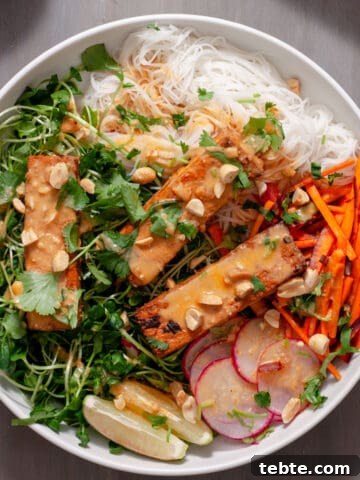 A white bowl with a summer roll salad topped with crispy peanut tofu, herbs, peanuts and peanut sauce.