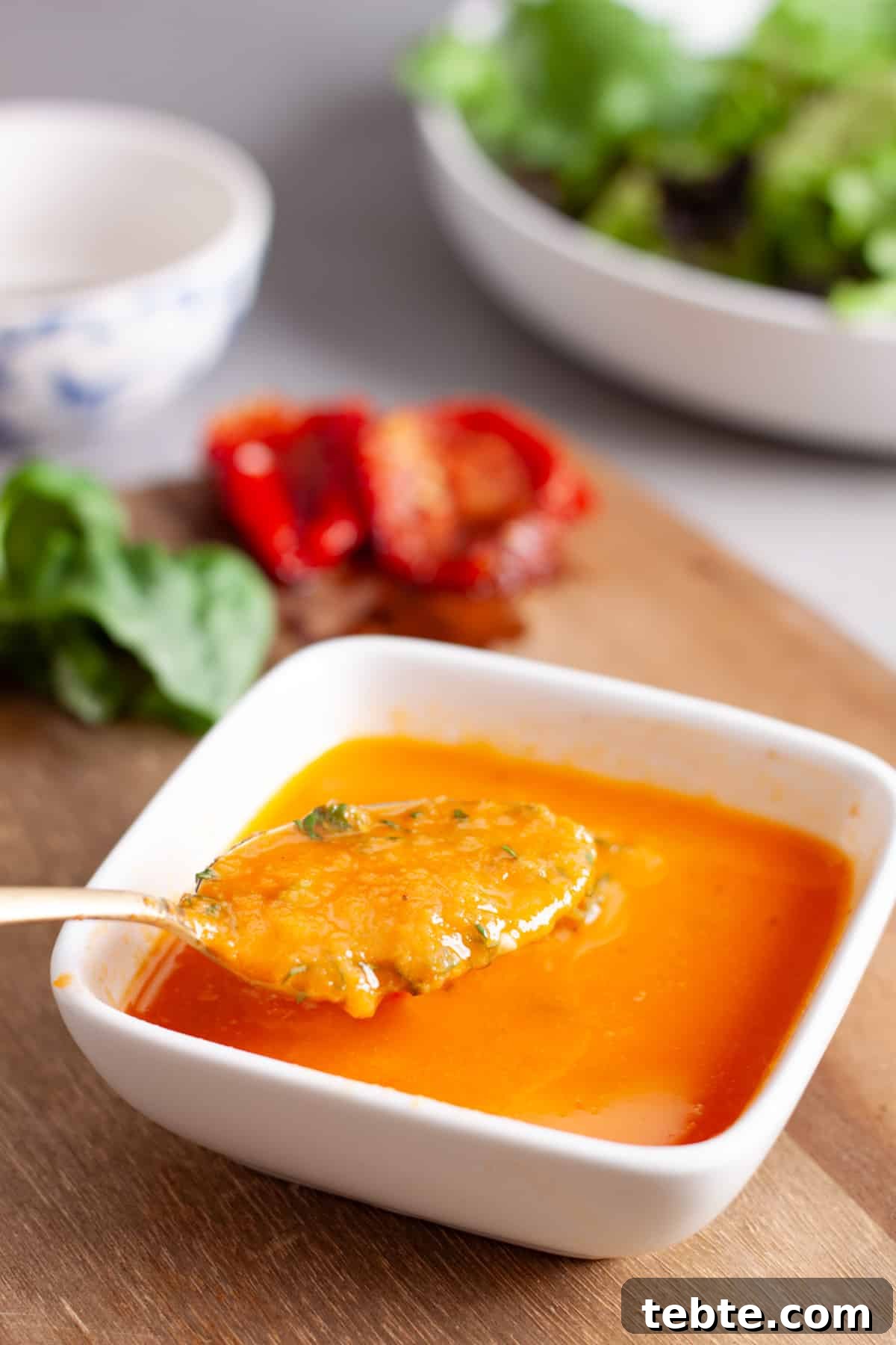 Sun-Dried Tomato Vinaigrette Recipe for Bright, Tangy Salads 8 A small white bowl of sun-dried tomato vinaigrette with a spoon taking some out and a bowl of greens in the background.