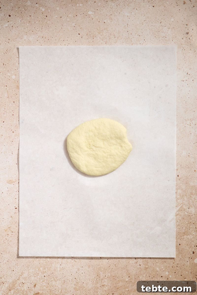 Crispy Sourdough Discard Crackers: Crunchy Homemade Recipe 6 Dough in a disk on a piece of parchment paper.