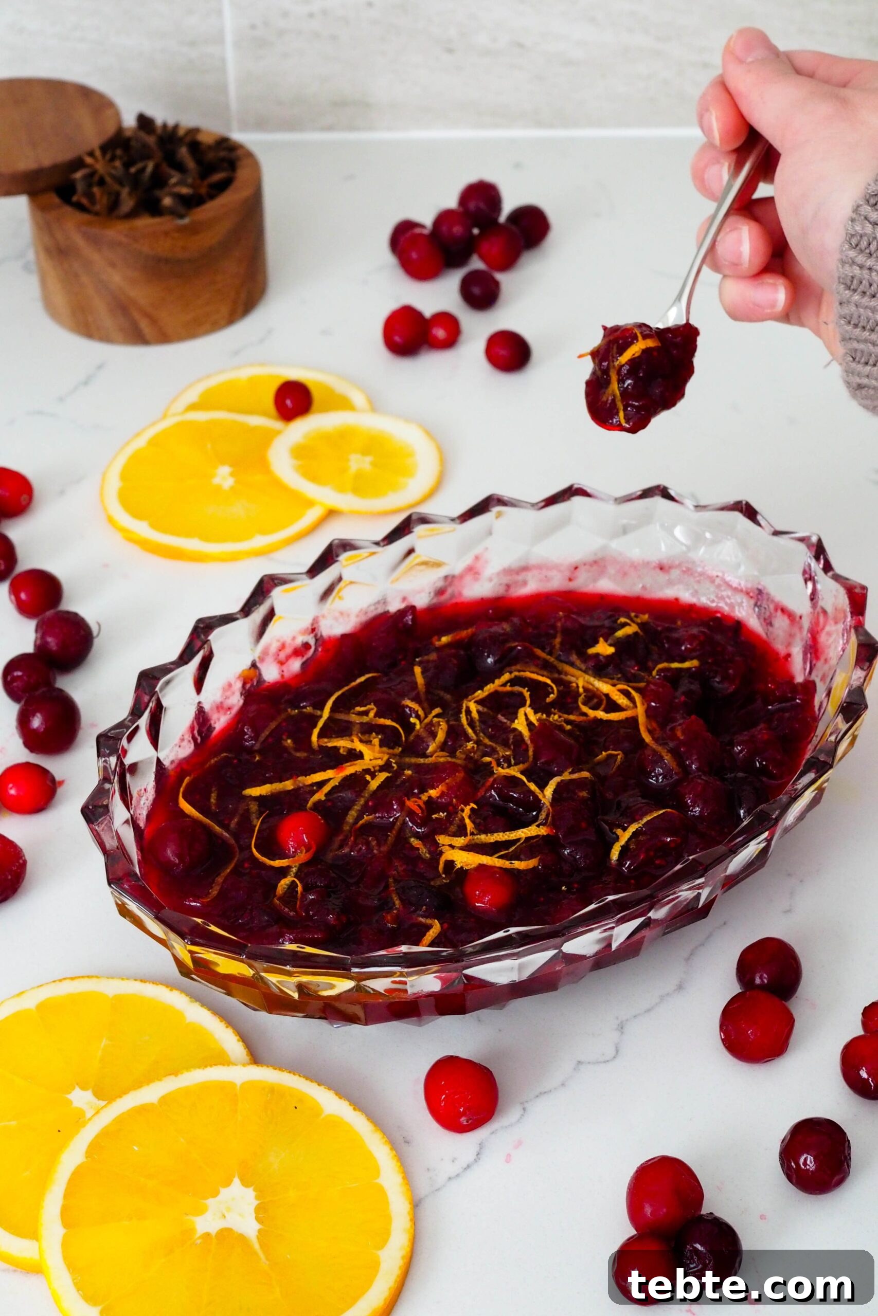 Classic Homemade Cranberry Sauce for Thanksgiving 2 A hand scoops a small serving of cranberry sauce out of a crystal serving dish.