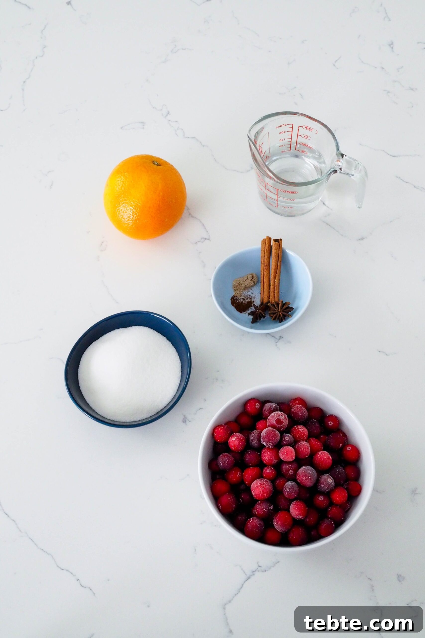Classic Homemade Cranberry Sauce for Thanksgiving 3 Frozen cranberries, sugar, an orange, spices, and water on a quartz counter.