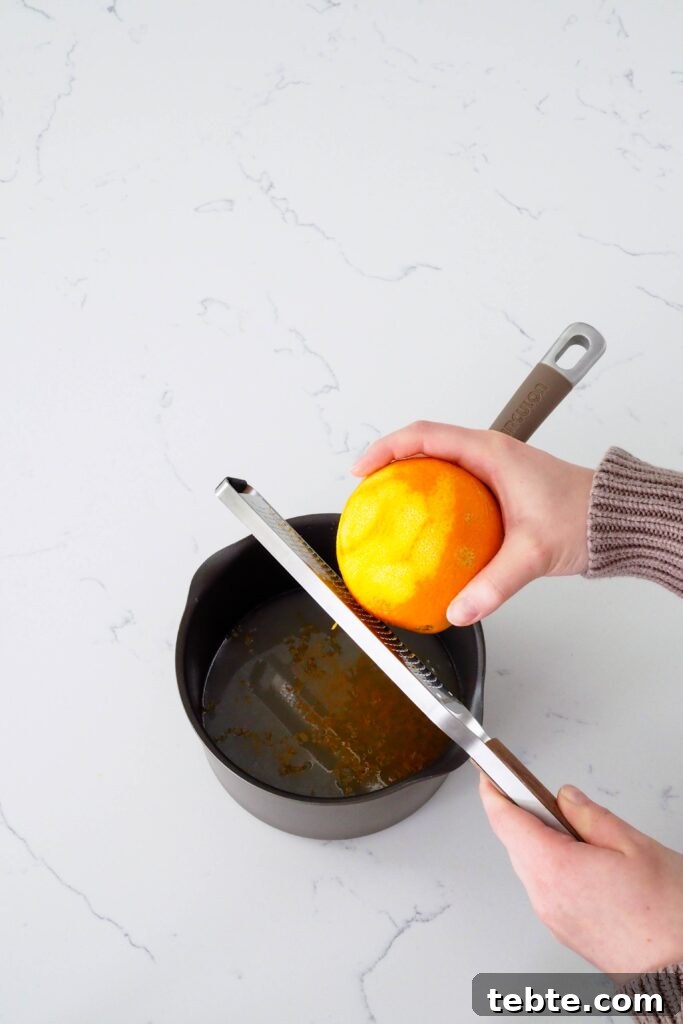 Classic Homemade Cranberry Sauce for Thanksgiving 4 Two hands zest an orange directly over a pot filled with water and sugar.
