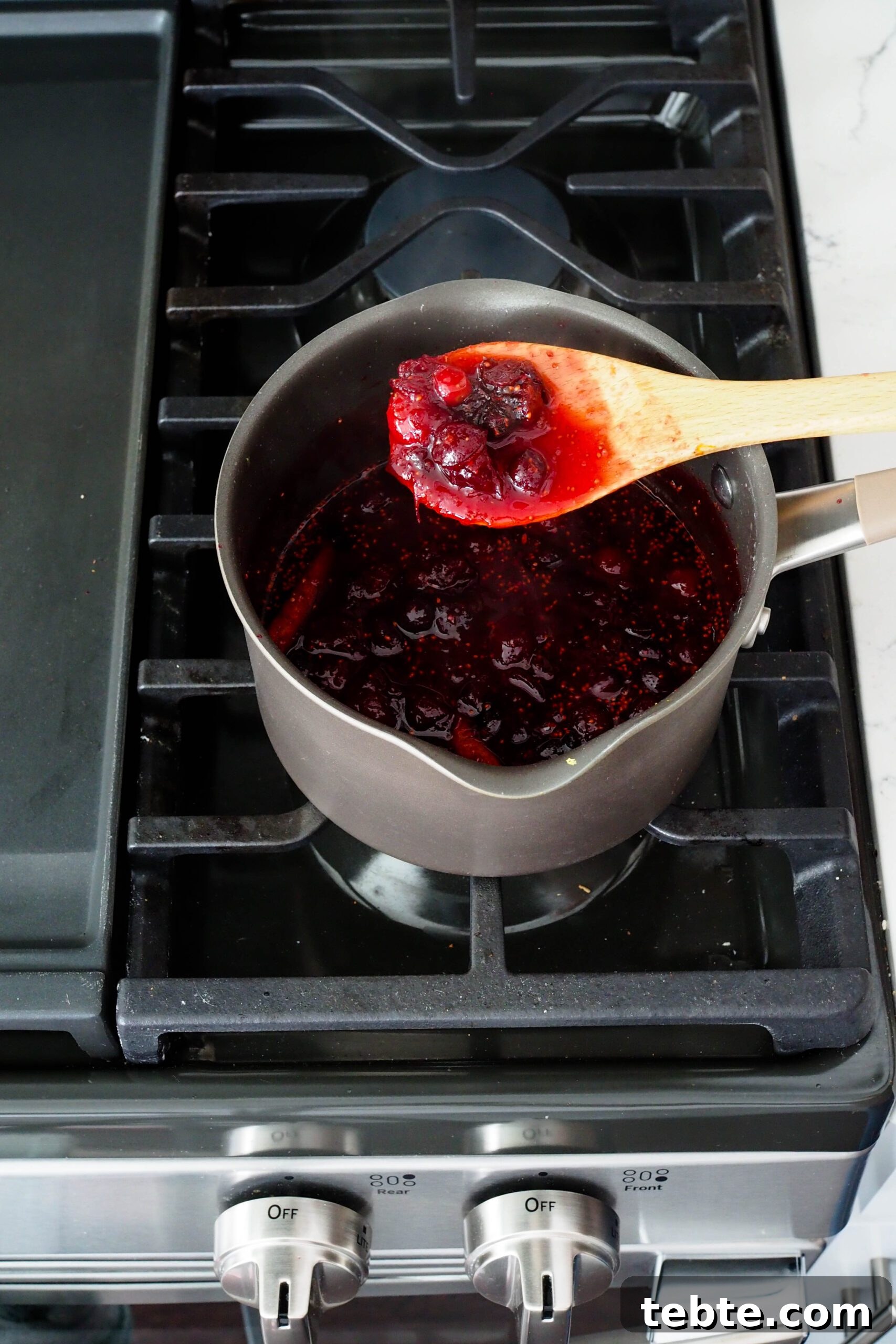 Classic Homemade Cranberry Sauce for Thanksgiving 6 A wooden spoon holds up some cranberry sauce.