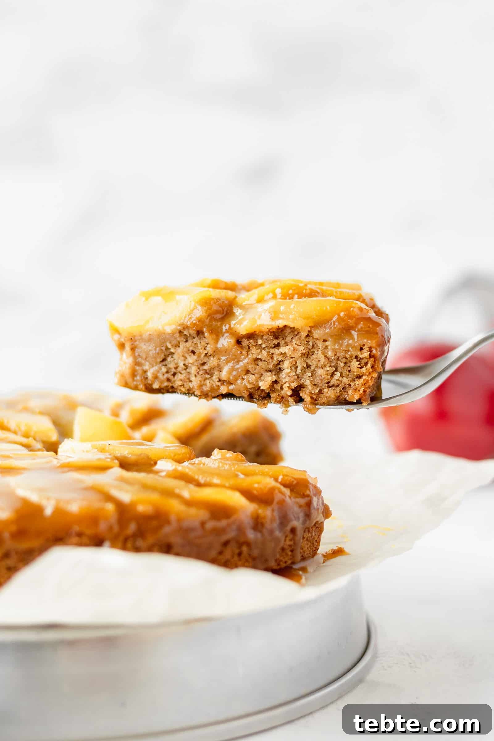 Moist Vegan Apple Cake Recipe with Cinnamon and Maple Glaze 2 A slice of vegan apple cake being lifted up.
