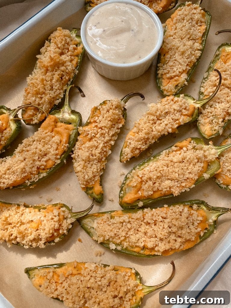 Gluten-Free Vegan Jalapeño Poppers: Creamy Dairy-Free Appetizer 2 jalapeno poopers with small bowl of ranch on parchmenet paper