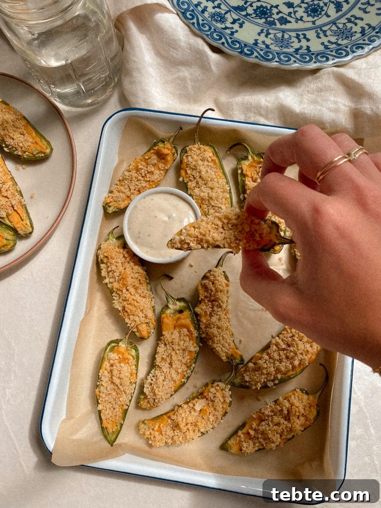 Gluten-Free Vegan Jalapeño Poppers: Creamy Dairy-Free Appetizer 3 hand dipping jalapeno popper in ranch with tray of jalapeno poppers