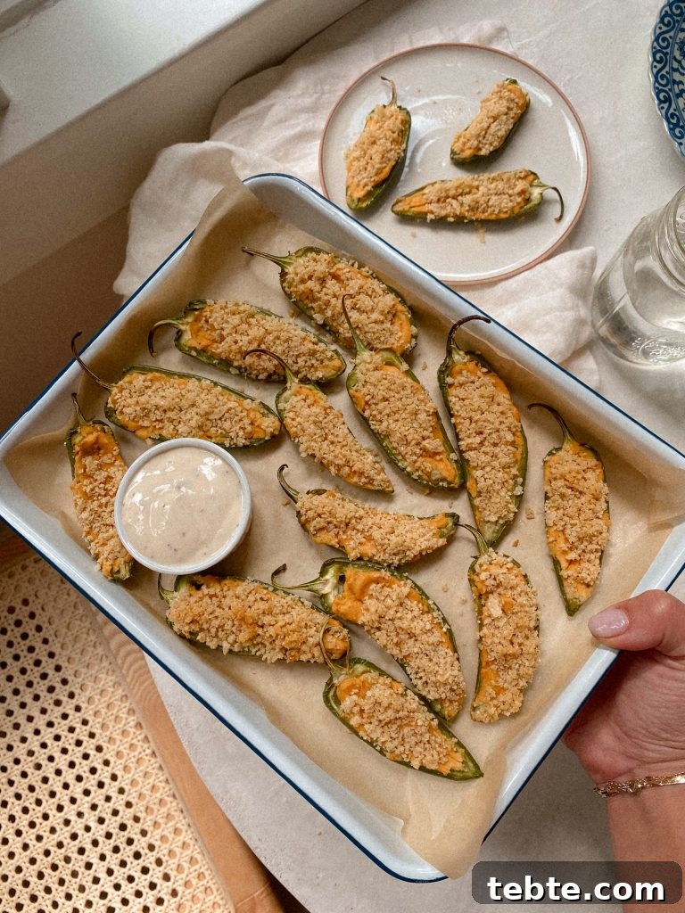 Gluten-Free Vegan Jalapeño Poppers: Creamy Dairy-Free Appetizer 5 hand holding tray of jalapeno poopers with small bowl of ranch on parchmenet paper