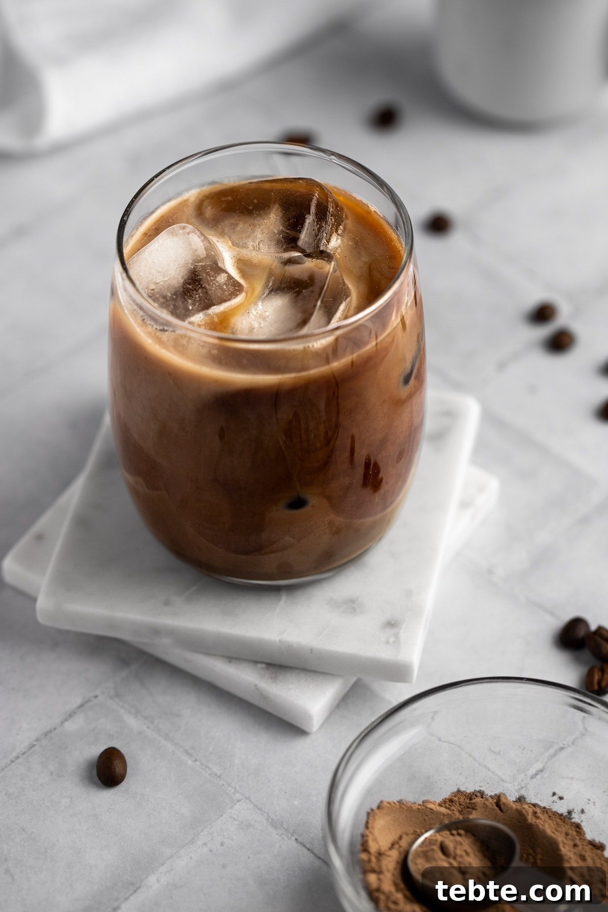 Protein Iced Coffee Recipe: High-Protein Chilled Coffee Drink 2 Overhead view of a glass of protein iced coffee sitting on two square white marble coasters.