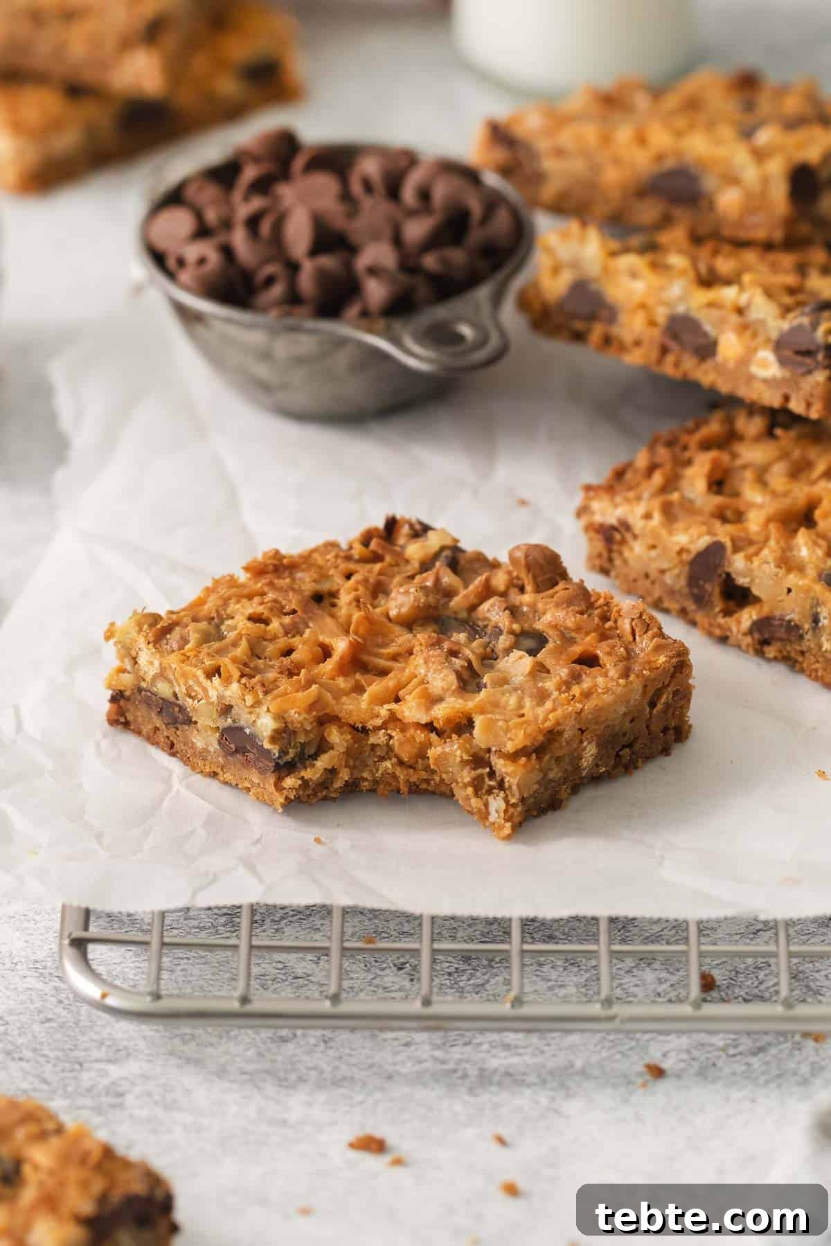 Gluten-Free 7-Layer Cookie Bars: Chewy Chocolate & Coconut Delight 11 7-layer bars on a cooling rack with bite taken out