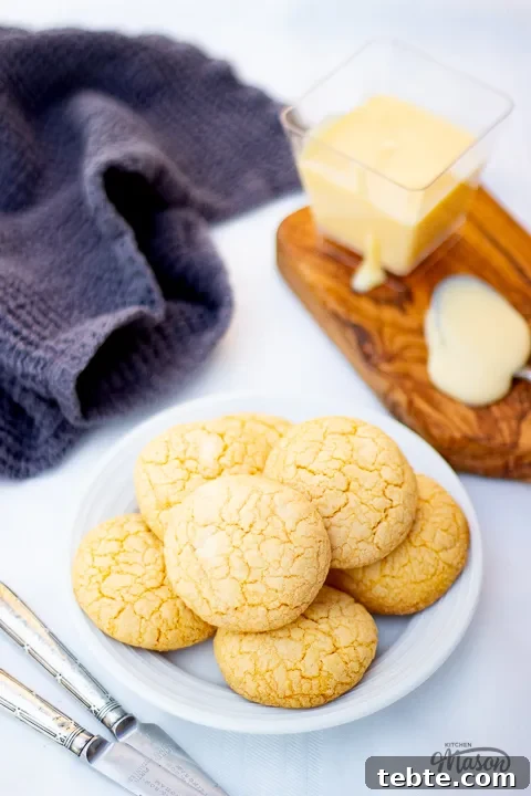 Custard and White Chocolate Cookies Recipe for Crisp, Creamy Treats 3 Custard and white chocolate biscuits on a plate with a small pot of custard and a teaspoon at the side.