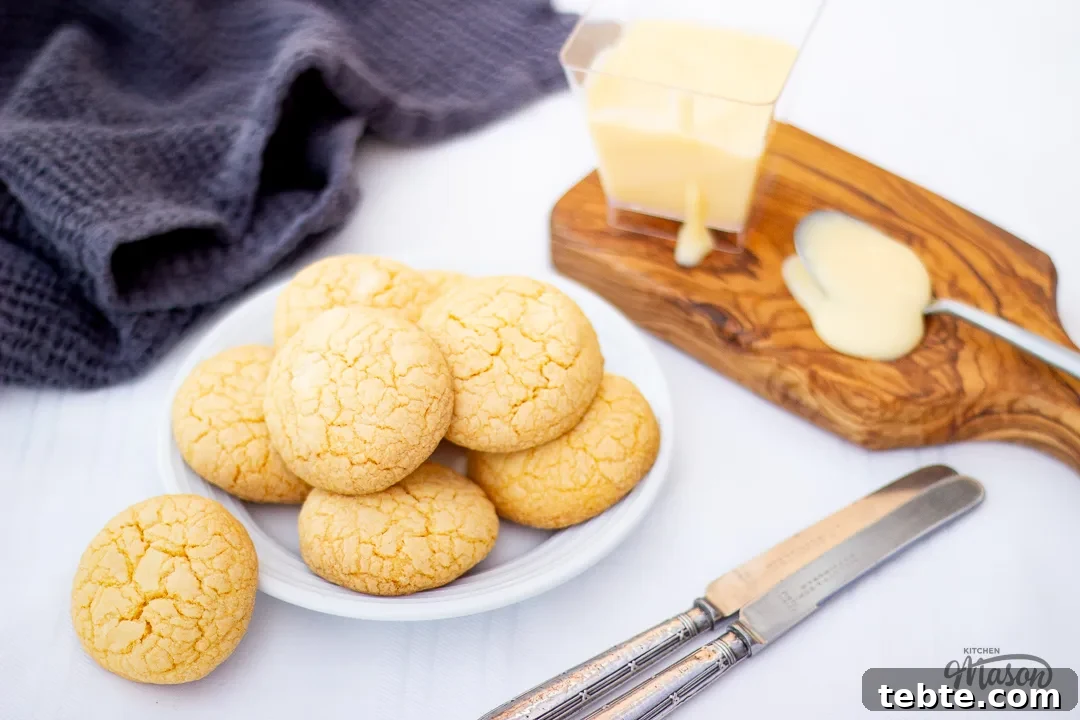 Custard and White Chocolate Cookies Recipe for Crisp, Creamy Treats 21 Custard and white chocolate biscuits on a white plate next to a pot of custard.