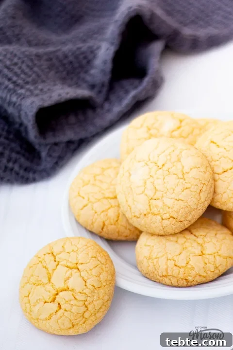Custard and White Chocolate Cookies Recipe for Crisp, Creamy Treats 4 Custard and white chocolate biscuits on a plate with a dark grey tea towel at the side.