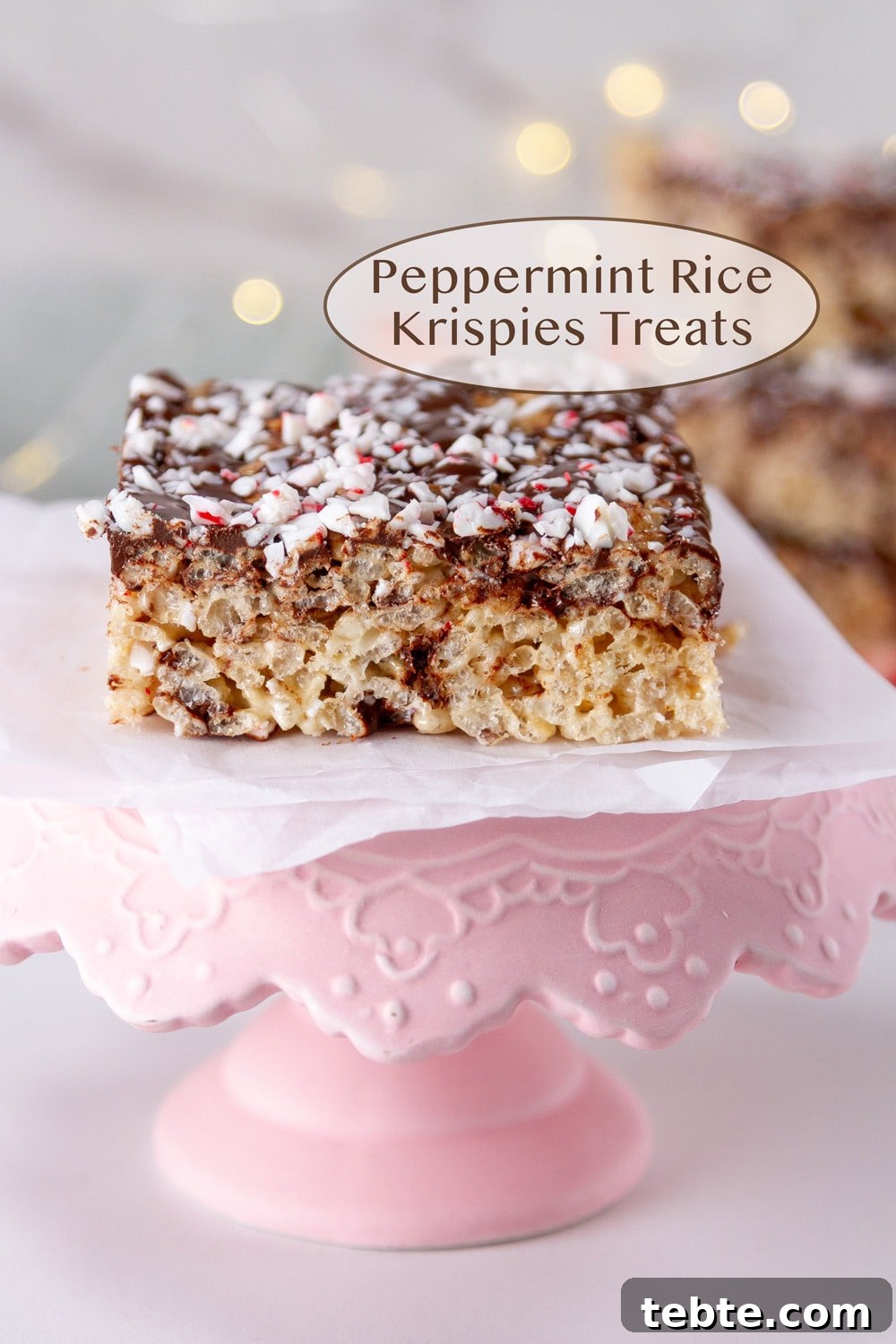 Peppermint Rice Krispies Treats Recipe for Festive Holidays 2 a Peppermint Rice Krispies Treats on a small pink serving tray with twinkle lights in the background.