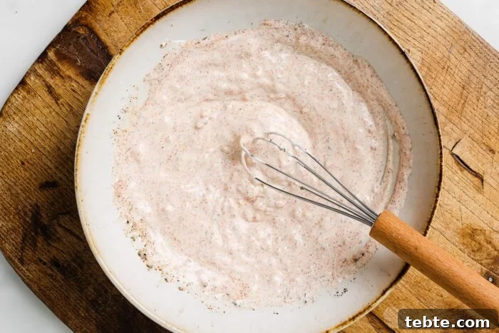 Creamy Yogurt-Marinated Chicken Breast Recipe 4 A bowl of creamy, light pink sauce—perfect for Yogurt Marinated Chicken Breast—speckled with seasoning is whisked with a metal whisk with a wooden handle, set on a wooden surface.