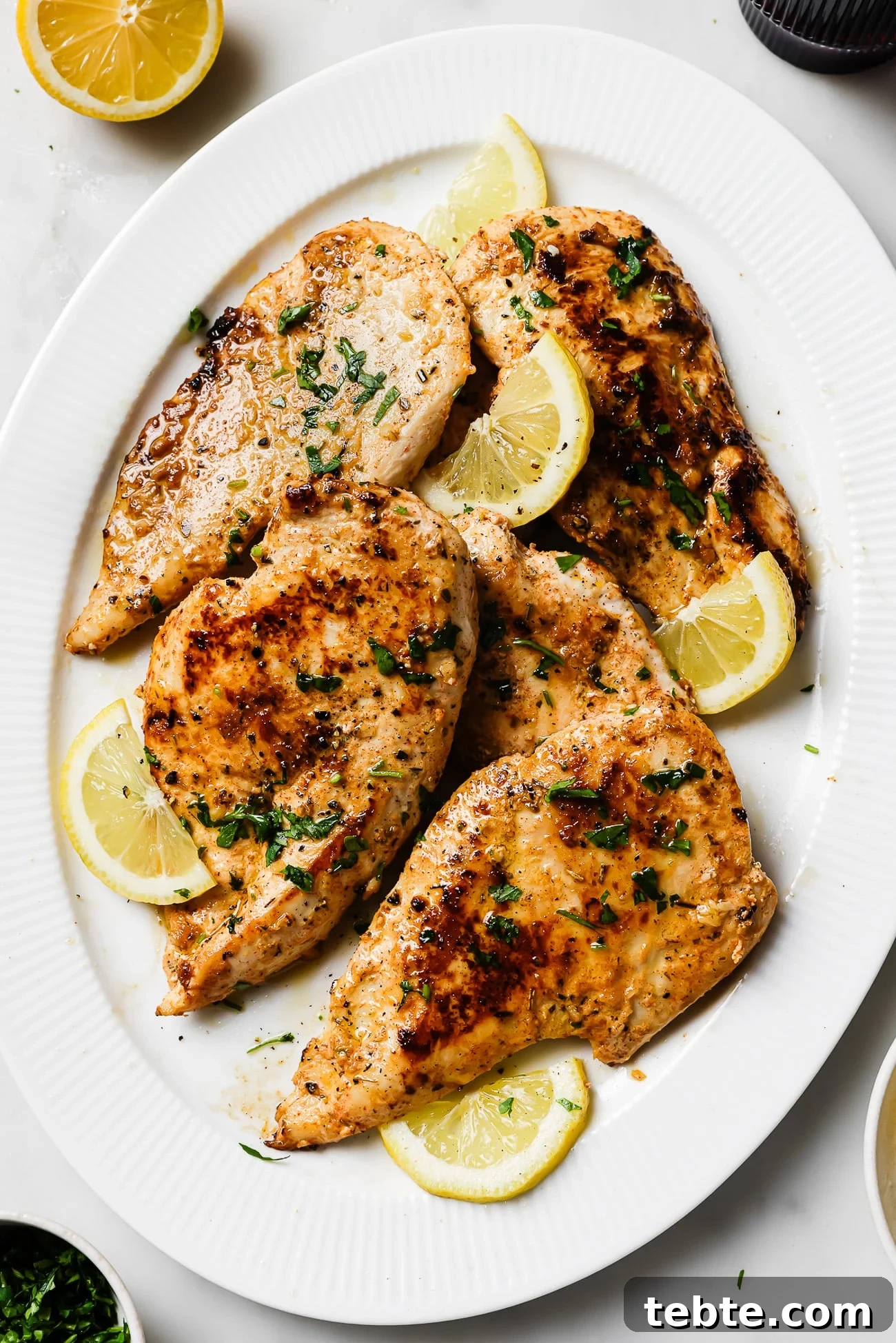Creamy Yogurt-Marinated Chicken Breast Recipe 8 Yogurt-marinated chicken breasts garnished with lemon slices and parsley on a white serving dish.
