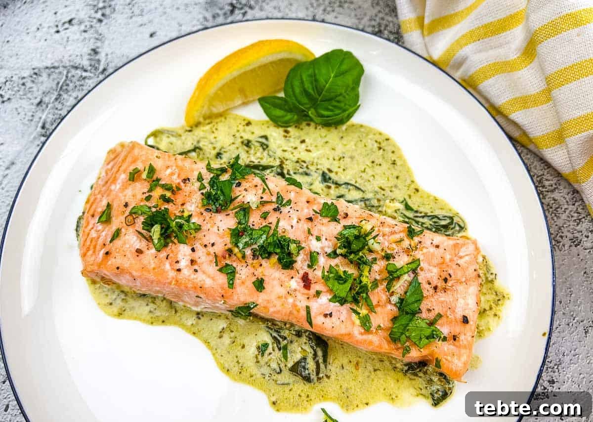 15 Easter Recipes Your Family Will Beg to Eat This Year 11 Baked Pesto Salmon with spinach sauce on a white plate.