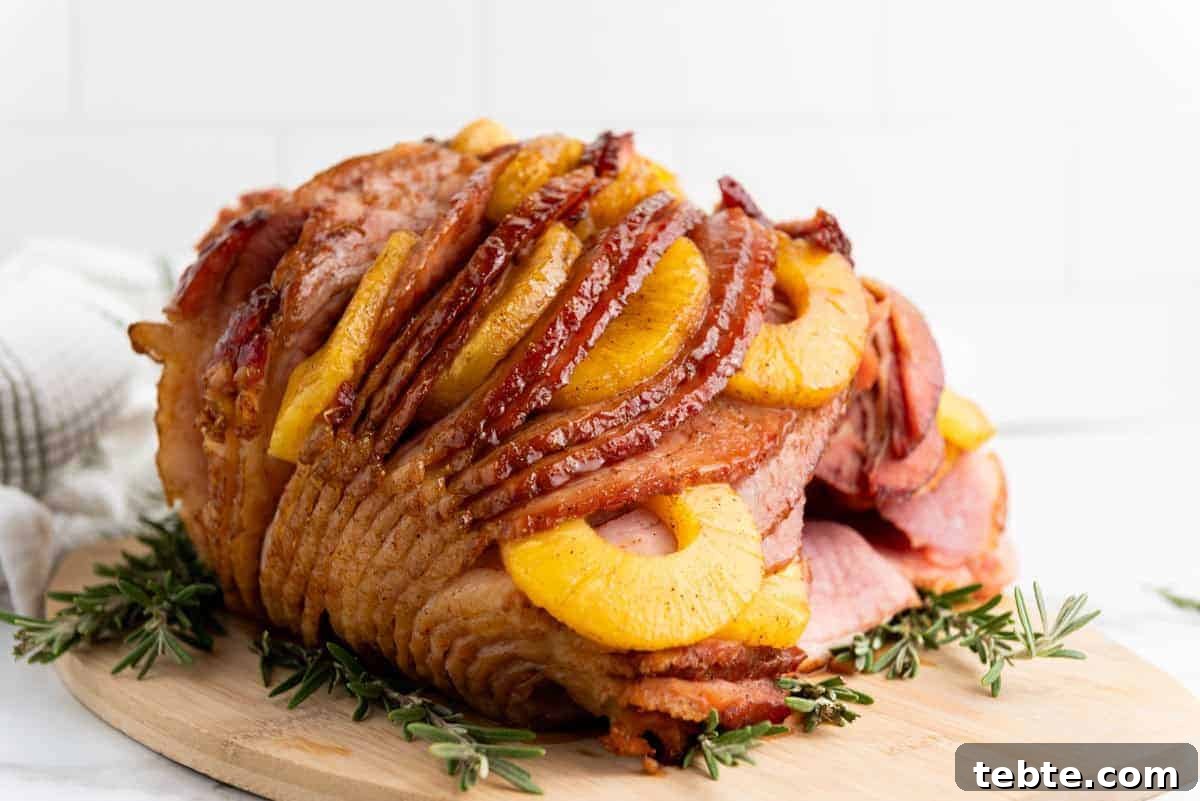 15 Easter Recipes Your Family Will Beg to Eat This Year 16 A Brown Sugar Pineapple Ham is placed on a wooden board, garnished with sprigs of rosemary.