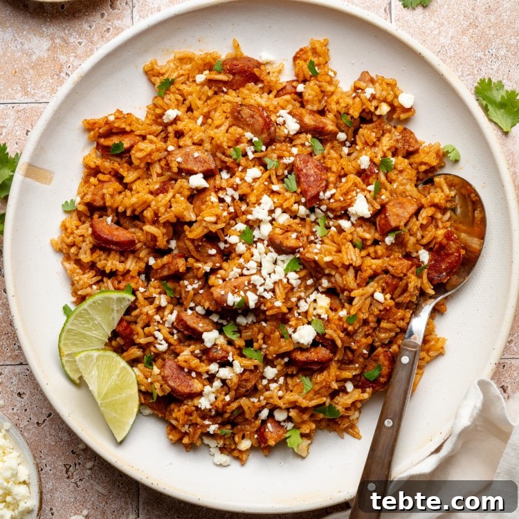 Spanish rice and chorizo on plate garnished with lime wedges and spoon on side of plate.