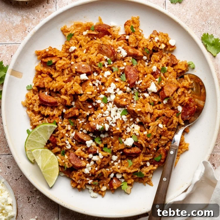 Spanish rice and chorizo on plate garnished with lime wedges and spoon on side of plate.