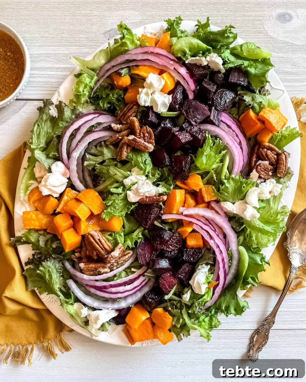 41 Fresh Fall Salad Recipes to Try This Season 13 A white platter on a yellow napkin filled with leafy greens, roasted beets and squash, red onions, pecans and chunks of goat cheese.