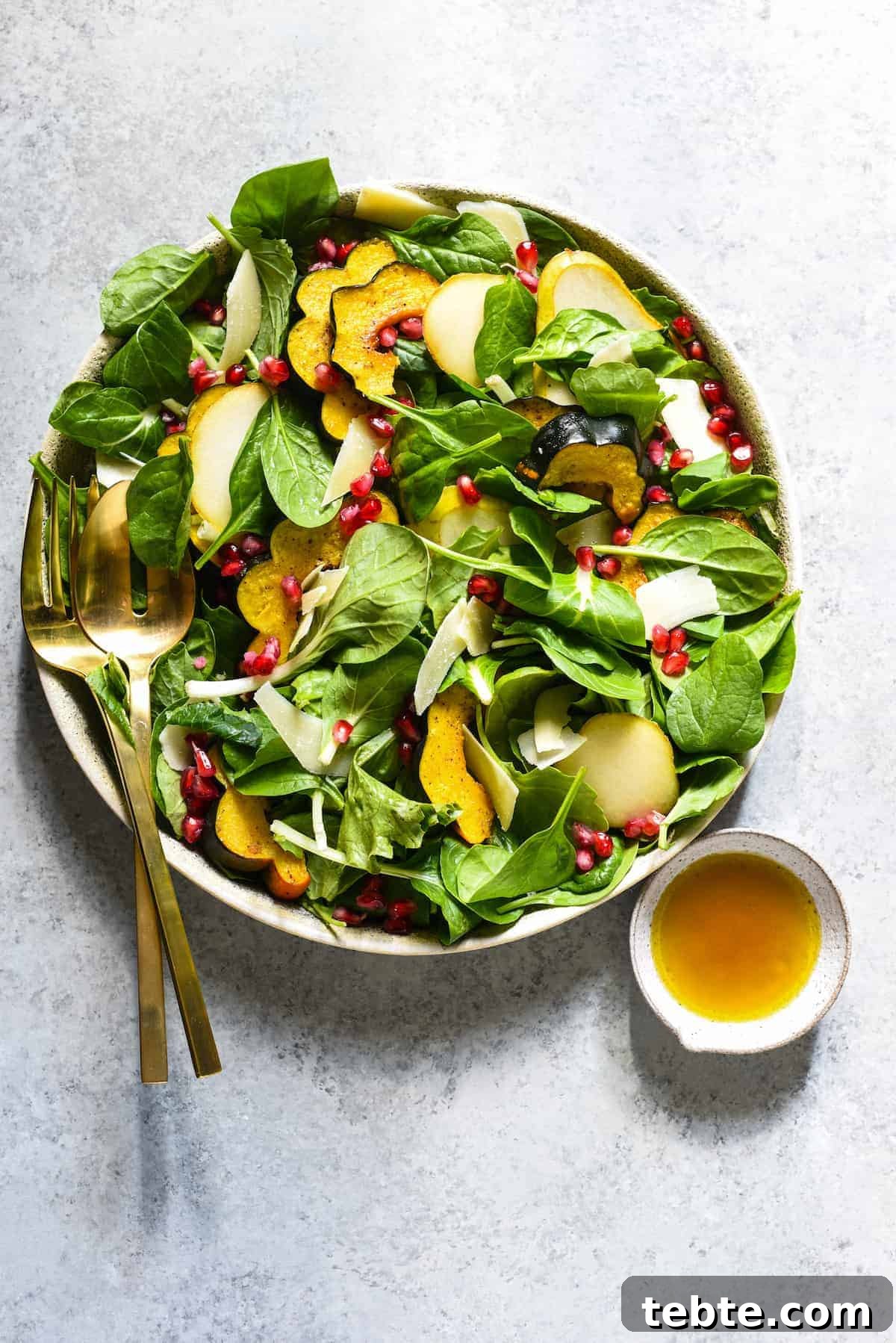 41 Fresh Fall Salad Recipes to Try This Season 14 A bowl of greens in a stone bowl, topped with sliced acorn squash and pomegranate seeds. A dish of dressing and gold utensils on the side.