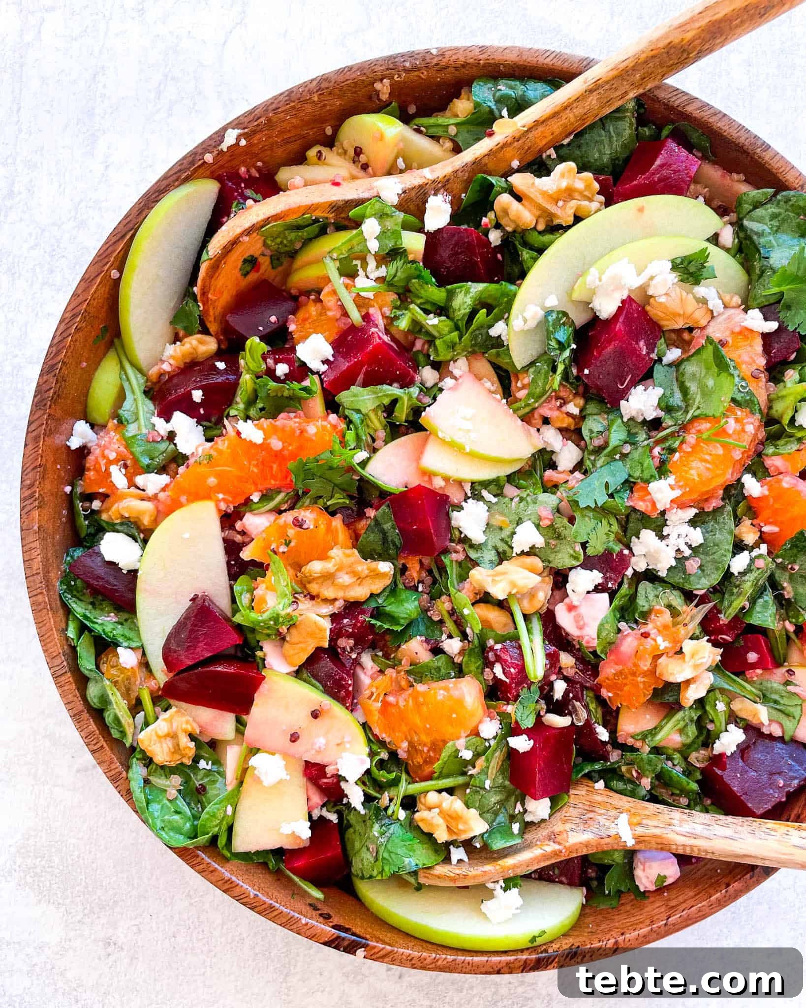 41 Fresh Fall Salad Recipes to Try This Season 19 A wooden bowl filled with leafy greens, sliced oranges, diced beets, sliced apples, nuts and topped with cheese crumbles. Two wooden spoons sit on opposite sides inside the bowl.