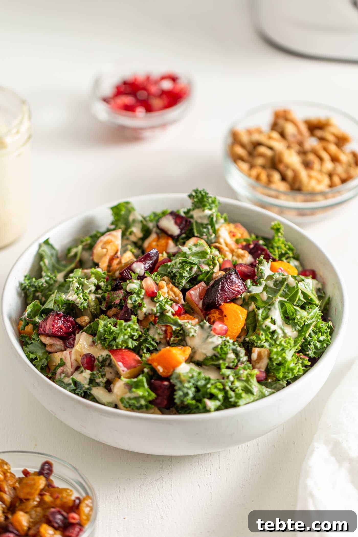41 Fresh Fall Salad Recipes to Try This Season 20 A white bowl filled with leafy green kale, topped with beets, squash, pomegranate seeds, diced apples, and nuts. A creamy tahini dressing is drizzled over the top and a bowl of nuts and a dish of pomegranate seeds sits above the salad.