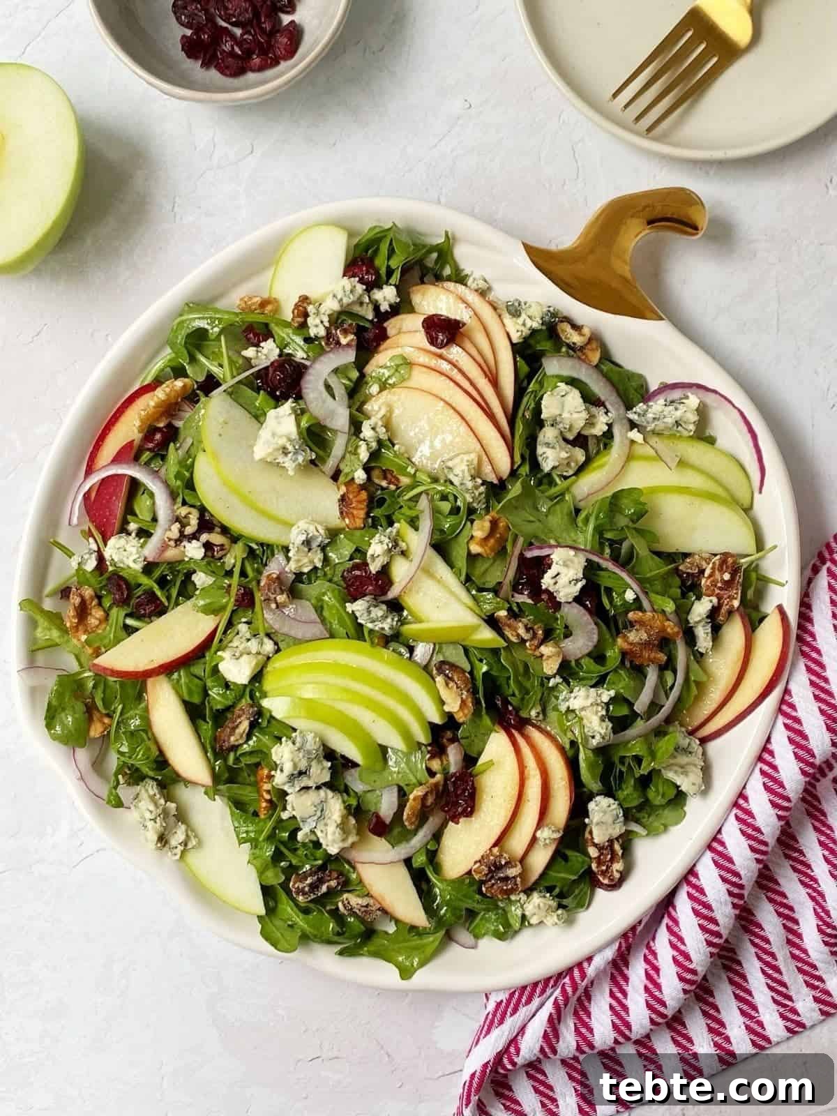 41 Fresh Fall Salad Recipes to Try This Season 29 Mixed greens on a white plate shaped like a pumpkin, with a gold stem. The salad is topped with sliced apples, cranberries, walnuts, blue cheese and red onions. A red napkin is off the the side, an extra apple, dried fruit and fork are in the background.