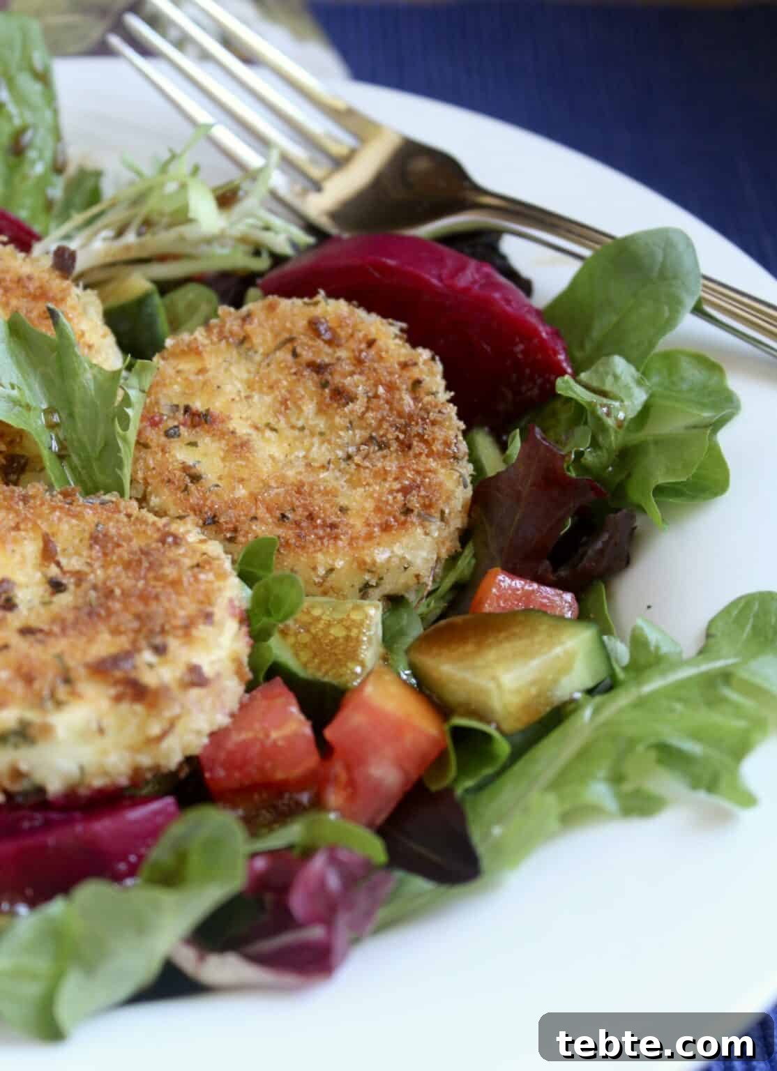 41 Fresh Fall Salad Recipes to Try This Season 30 An up close photo of salad greens topped with sliced beets, diced cucumbers, tomatoes, and topped with three breaded rounds of goat cheese. The salad is served on a white plate with a fork to the side.