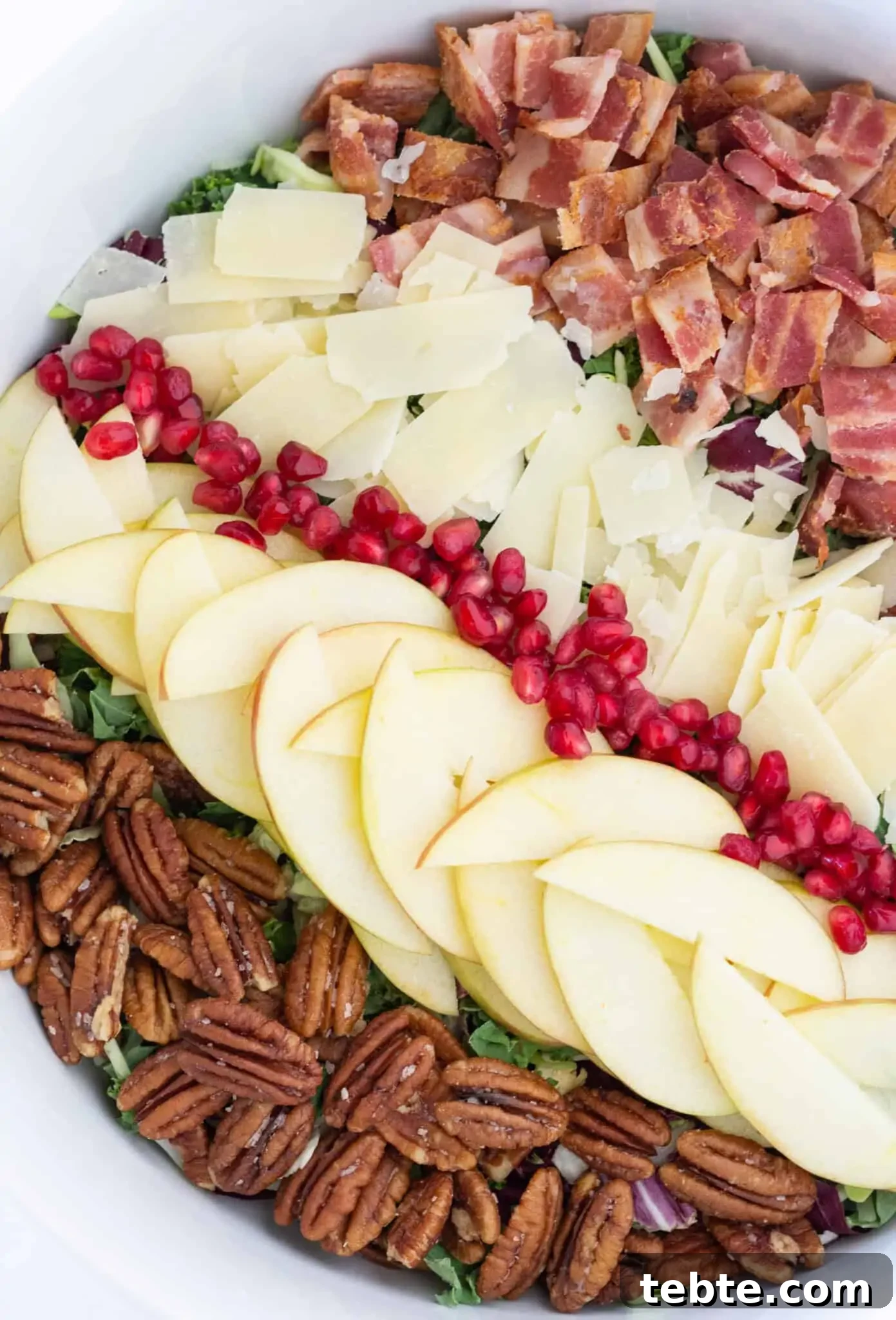 41 Fresh Fall Salad Recipes to Try This Season 33 Ingredients arranged on a bed of greens on a white platter starting from left to right: pecan halves, sliced apple, pomegranate seeds, shaved parmesan, diced bacon.