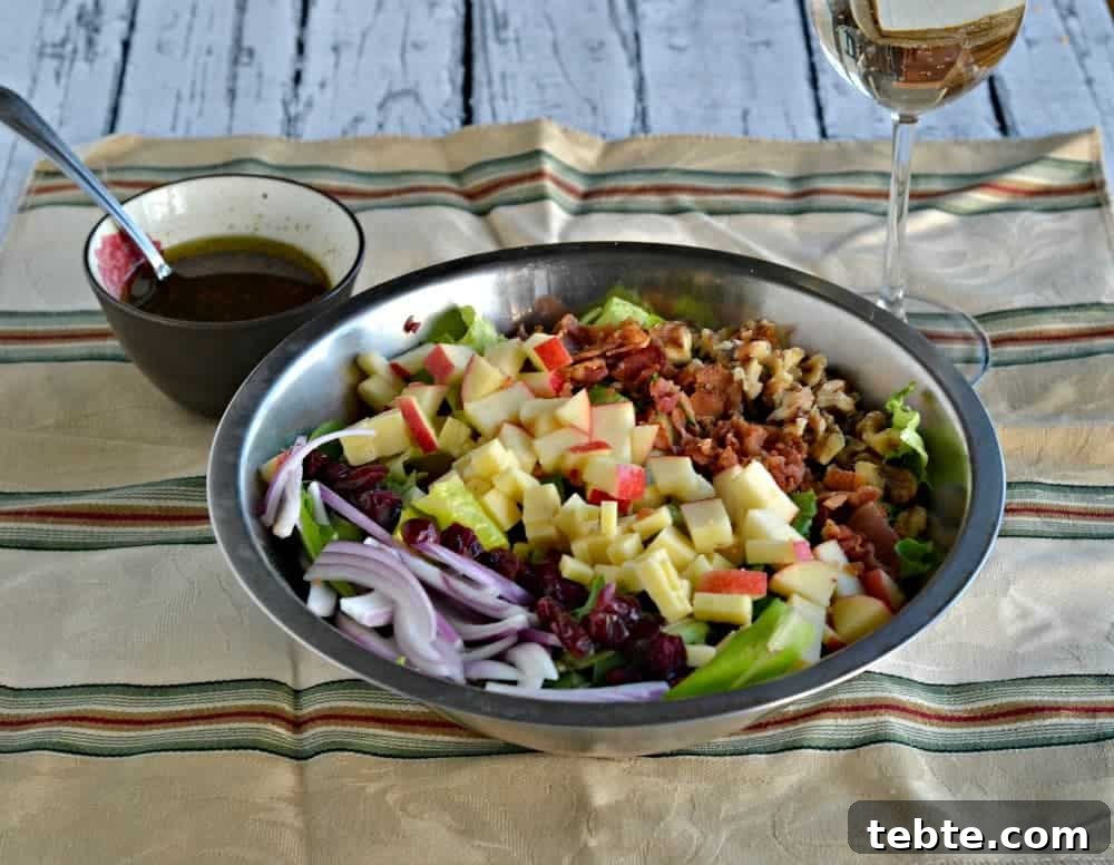 41 Fresh Fall Salad Recipes to Try This Season 39 A salad sitting in a stainless bowl, filled with diced apples, diced cheddar, nuts, greens, dried cranberries and sliced onions. The bowl is sitting on a yellow napkin with colorful stripes, a glass of white wine in the background and extra dressing in a dish next to the salad.