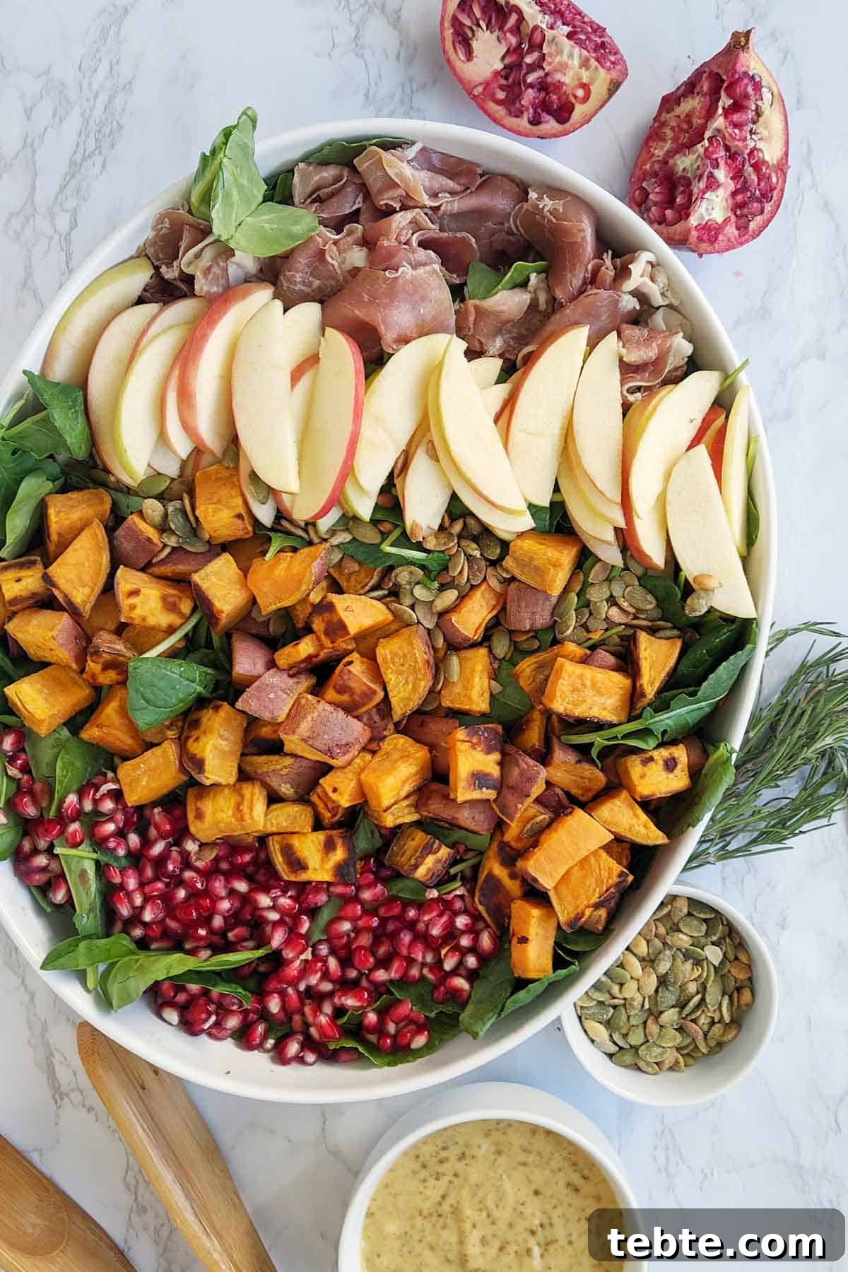 41 Fresh Fall Salad Recipes to Try This Season 6 Pomegranate seeds, sweet potatoes, sliced apples, pumpkin seeds, prosciutto sitting on a bed of greens in a white dish