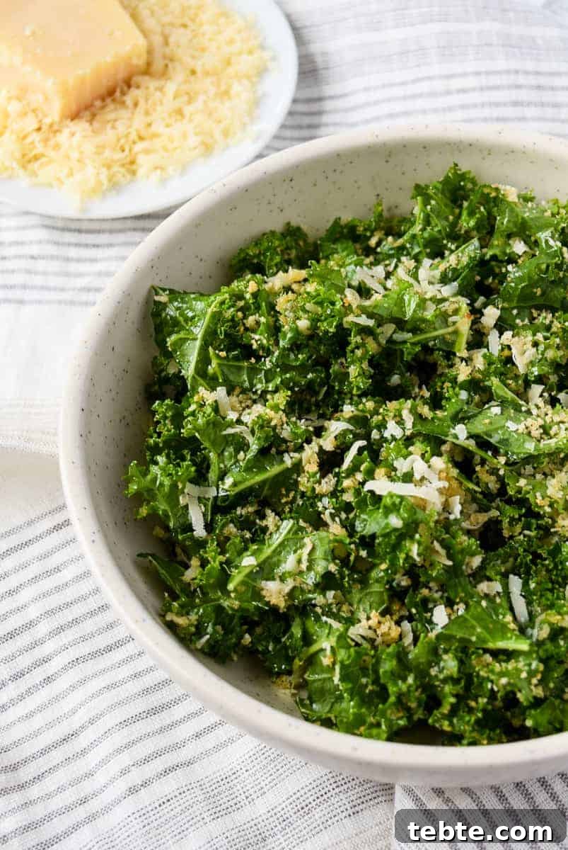41 Fresh Fall Salad Recipes to Try This Season 9 Green leafy kale in a white bowl topped with shredded parmesan cheese and toasted breadcrumbs. Parmesan cheese in a bowl sits in the background.