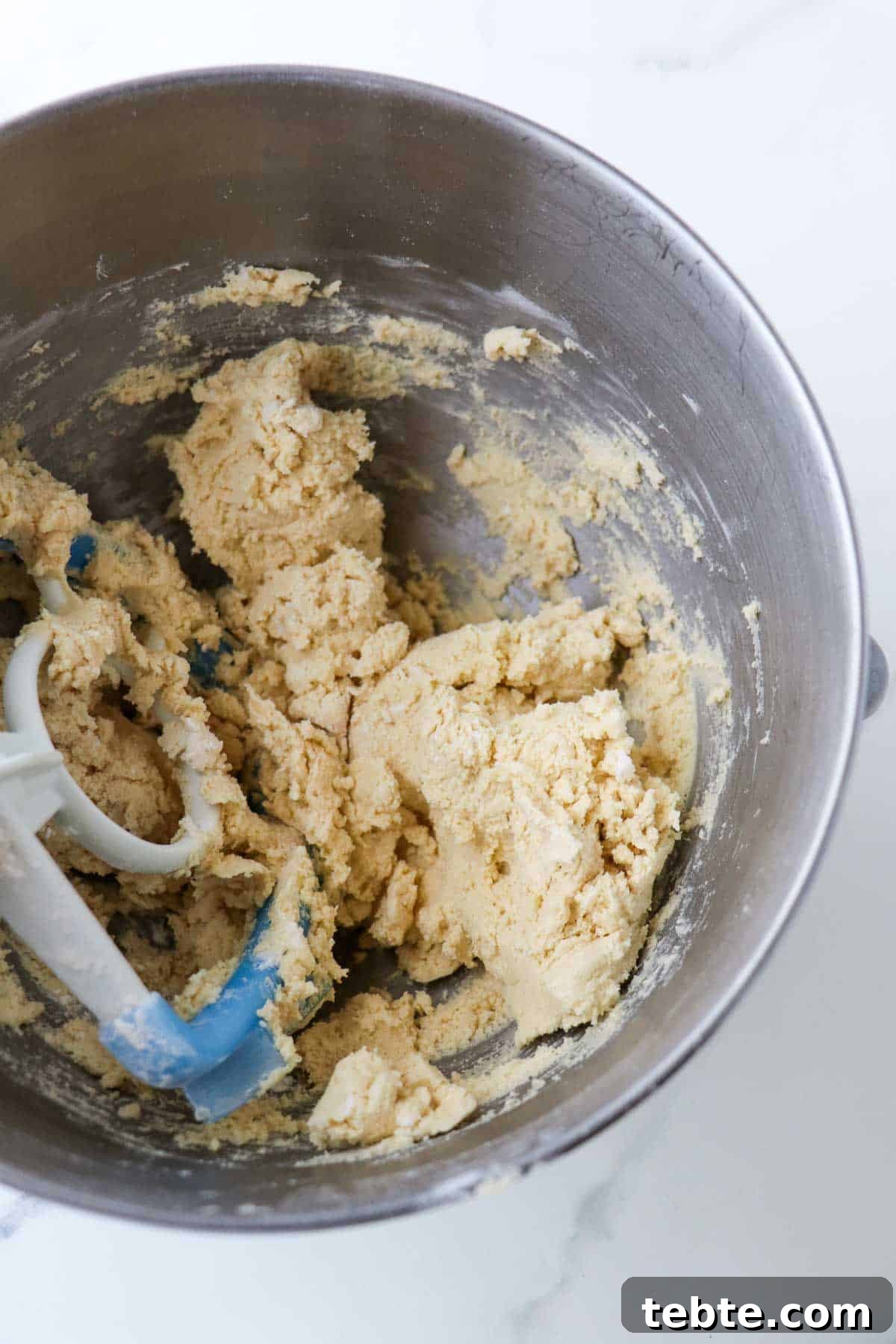 Vanilla cookie dough in a metal bowl with a paddle attachment.