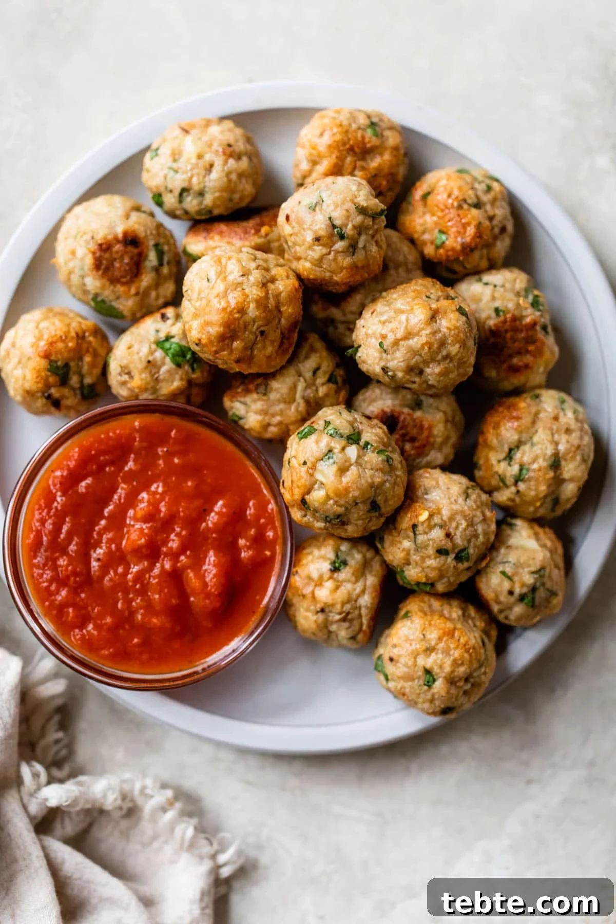 Crispy Baked Chicken Meatballs with Garlic Herb Sauce 2 a plate filled with meatballs and a small bowl of marinara sauce