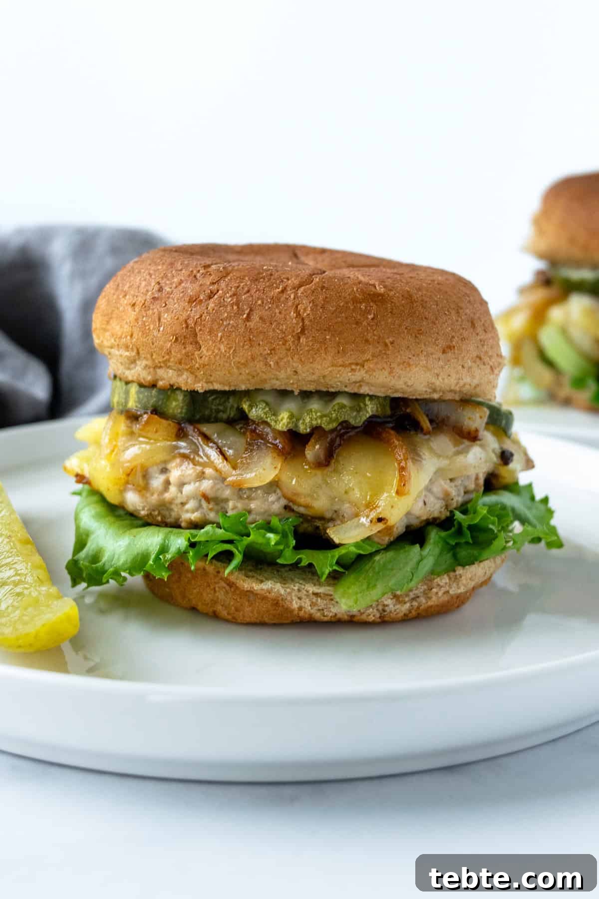 Juicy Turkey Smash Burgers with Crispy Edges and Melty Cheese 2 Turkey Smash Burger on a bun with lettuce and pickles served on a white plate.