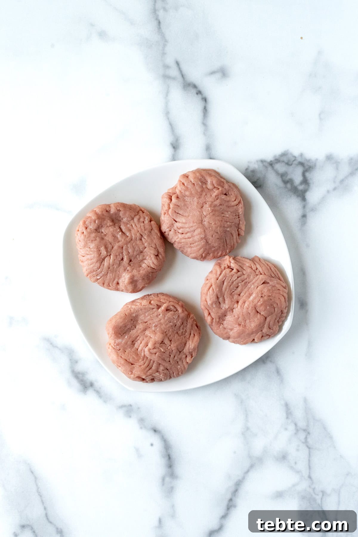 Juicy Turkey Smash Burgers with Crispy Edges and Melty Cheese 4 Raw Turkey Burgers on a White Plate.
