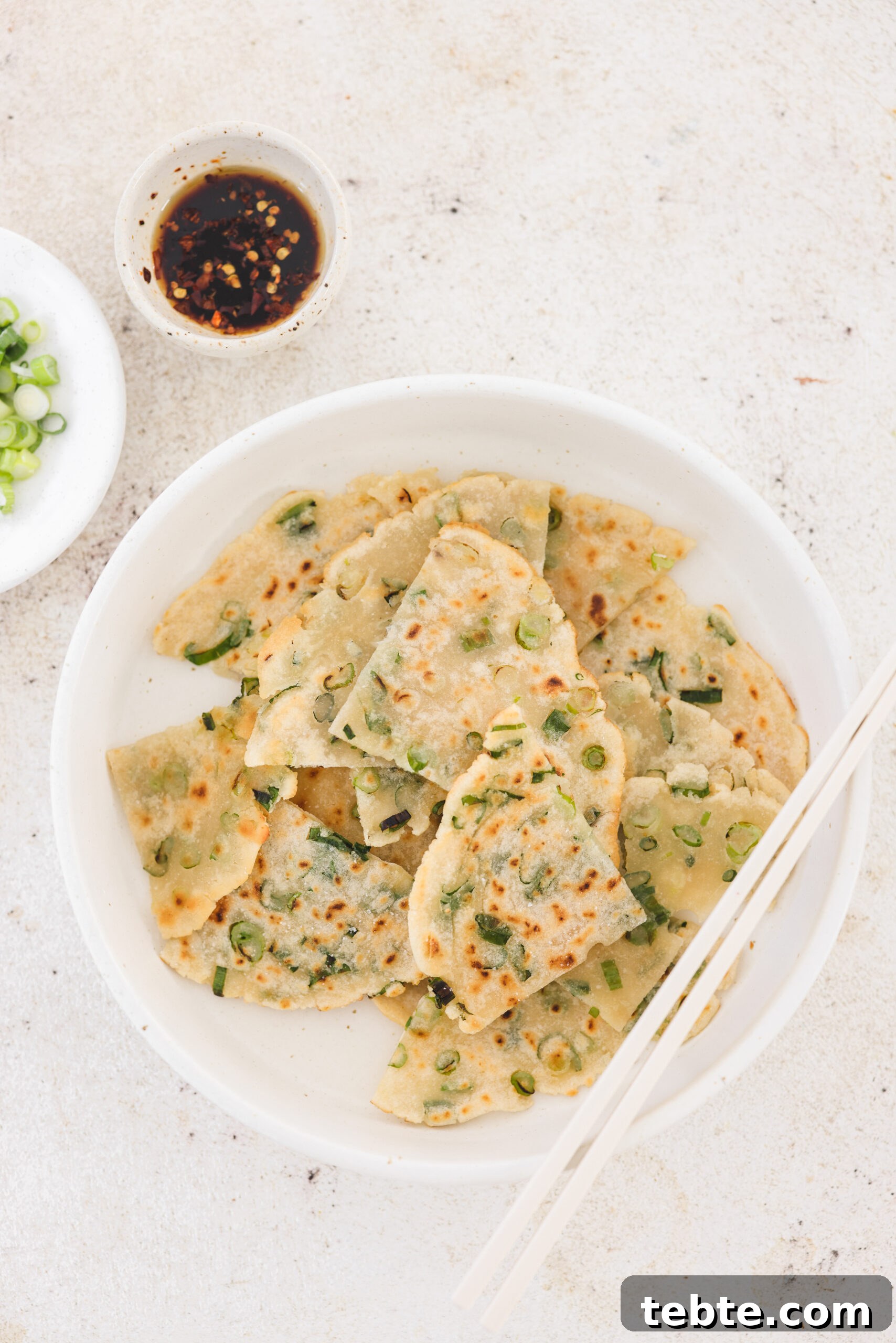 an overhead shot of scallion pancakes in a white dish with chopsticks resting on the side. 