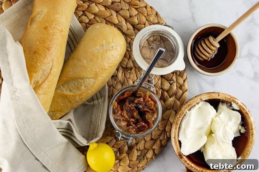 two baguettes with a bowl of creamy cheese, beside a jar of bacon jam, a bowl of honey, and a lemon