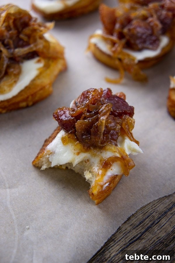 a bacon jam crostini with a bite taken out of it on a parchment paper with other crostinis around it.