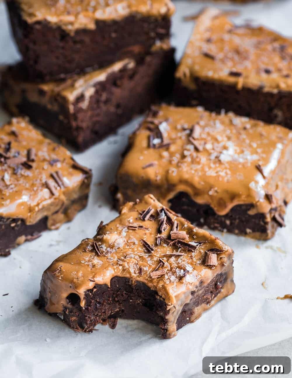 Vegan Gingerbread Brownies with Espresso Glaze Recipe 3 5 brownies on parchment paper, one with a bite taken from it.