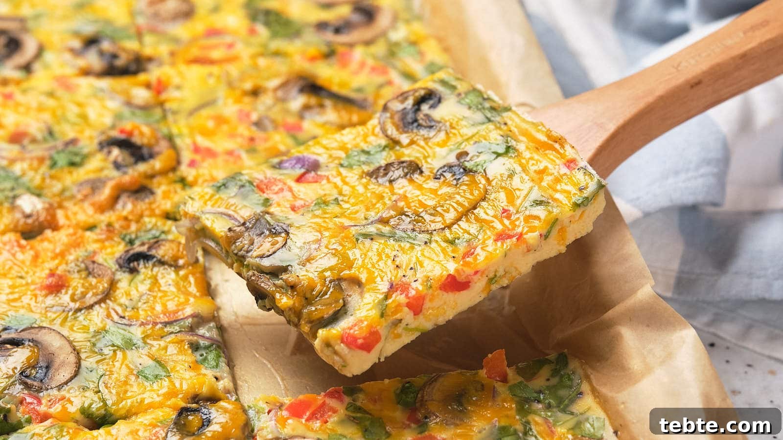 13 High-Protein Game Day Breakfasts to Fuel Your Morning 4 A square slice of sheet pan omelet on a wooden spatula above parchment paper.