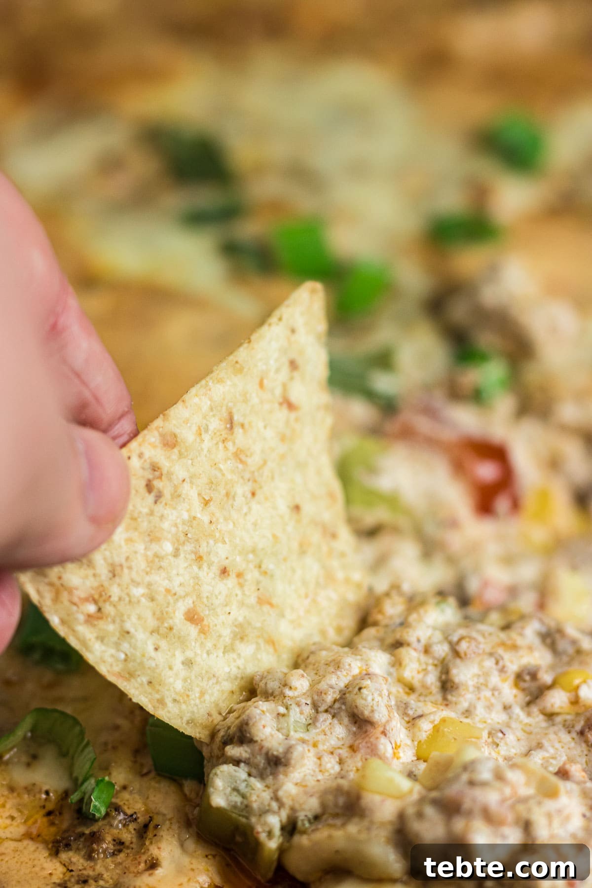 Savory Baked Cowboy Dip Recipe for Parties and Game Day 6 A tortilla chip being dipped into the cowboy dip.