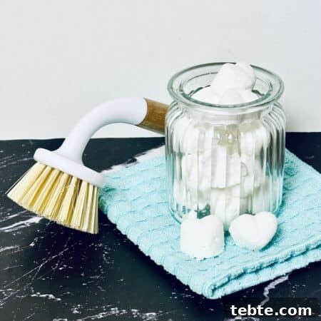 Homemade Dishwasher Pods in a glass cup, with a cleaning brush next to it.
